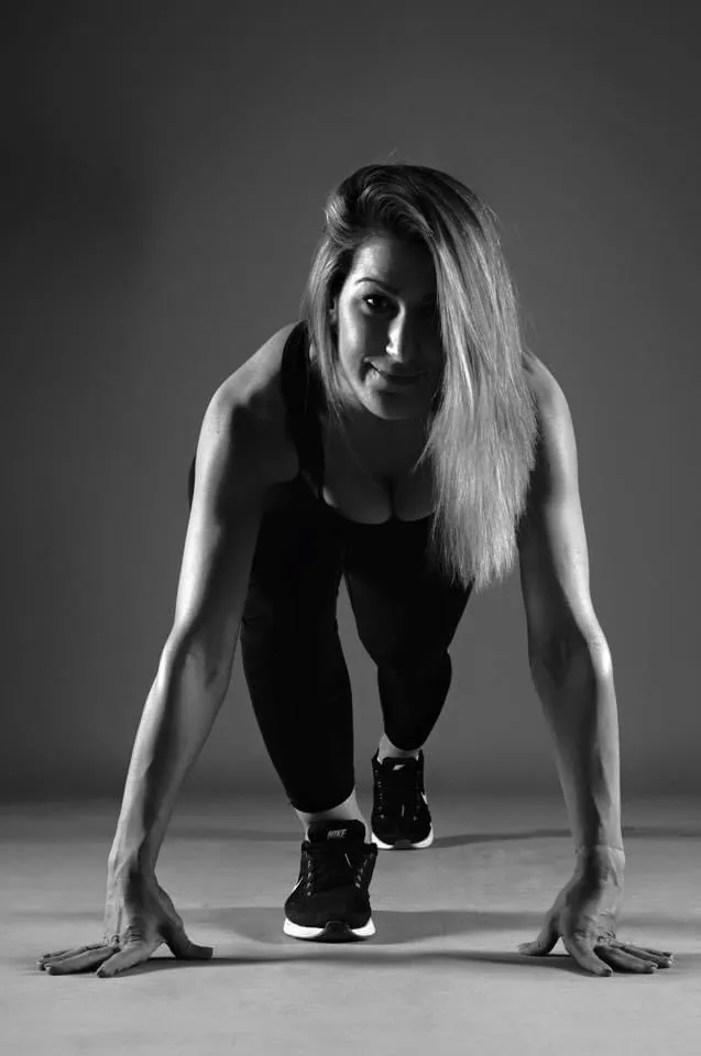 Portrait en noir et blanc de Clémence Baslé, coach sportive, en position de départ, les mains au sol