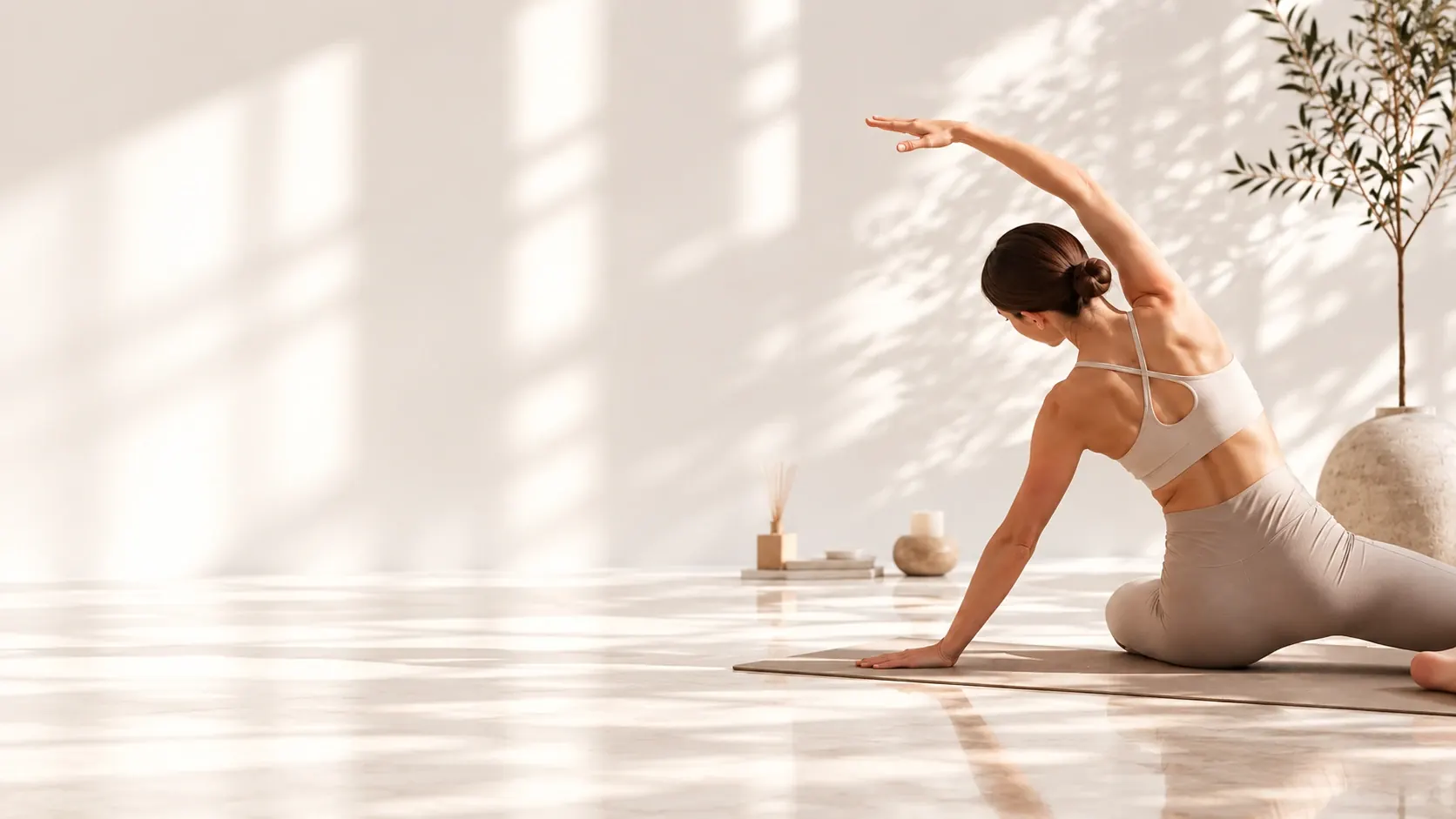Femme en tenue beige faisant un étirement latéral de Pilates sur un tapis, dans un studio baigné de lumière naturelle